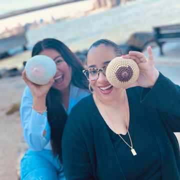 Two women holding crocheted breast models and smiling.