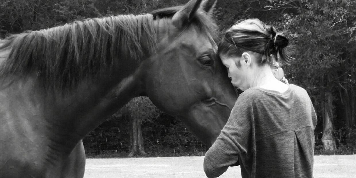 A woman shares a quiet moment with a horse in a black-and-white photo.