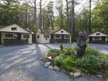 Cabins with bear decorations surrounded by trees and a bear statue in a garden area.