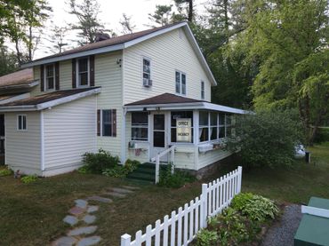 A quaint yellow house with an office and vacancy sign, surrounded by greenery.