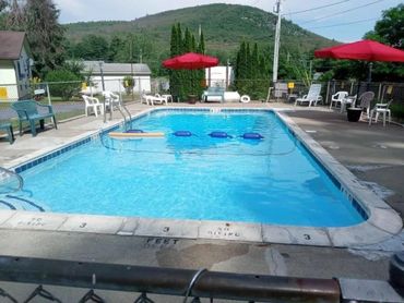 Outdoor swimming pool with red umbrellas and white chairs in a peaceful setting.