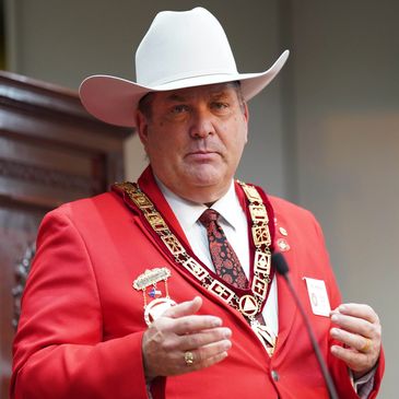 Man in a red blazer and white cowboy hat with ceremonial chain.