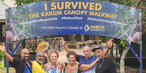 Group of six happy people posing under a Kakum Canopy Walkway sign.