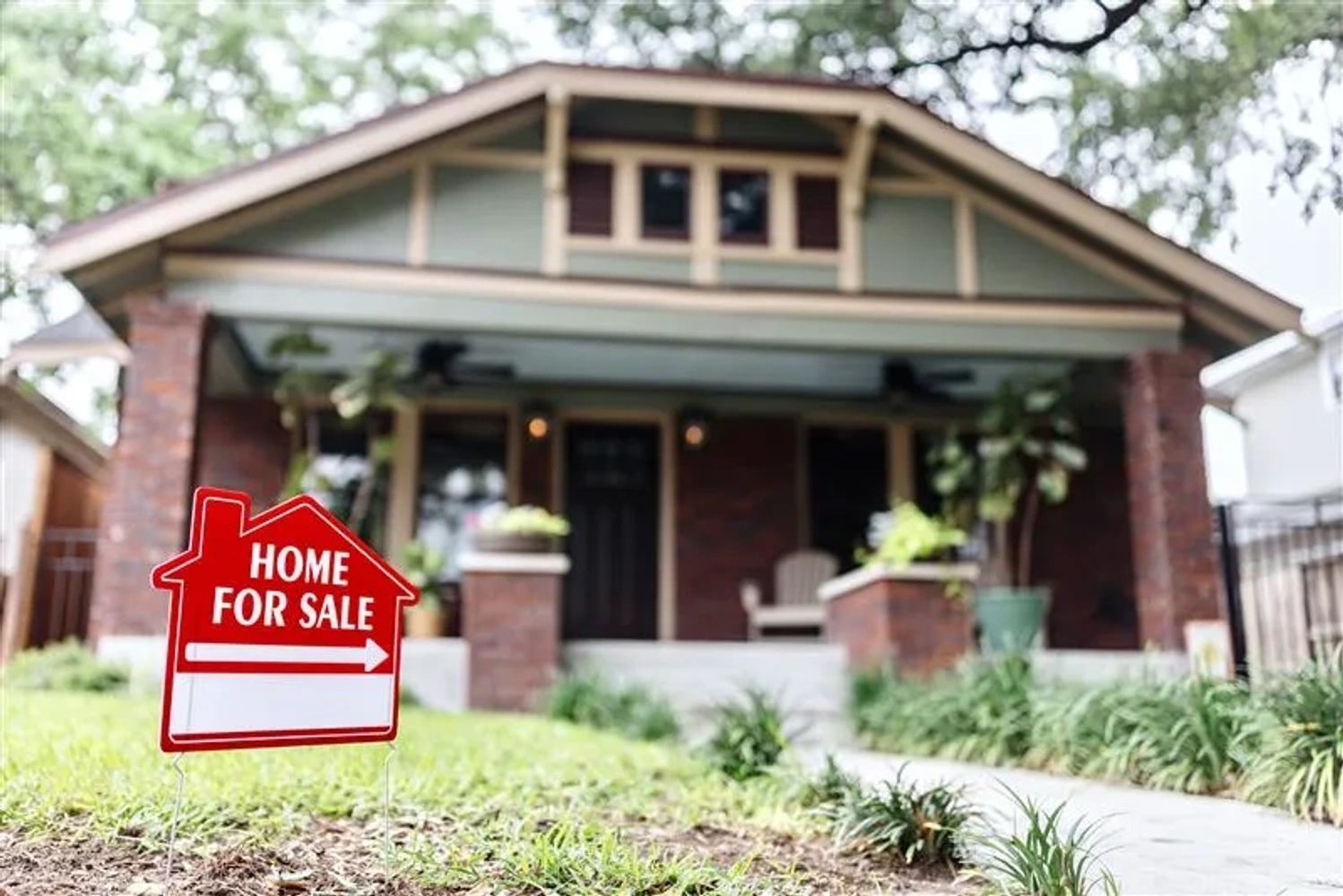 Red 'Home for Sale' sign in front of a cozy house with a porch.