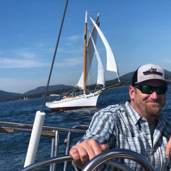 Man steering sailboat with another sailboat in the background.