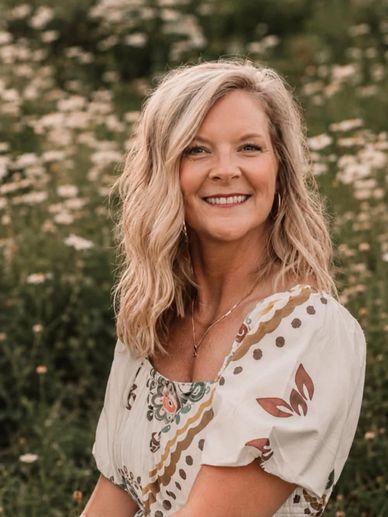 Smiling woman in floral dress outdoors with wildflowers in background.
