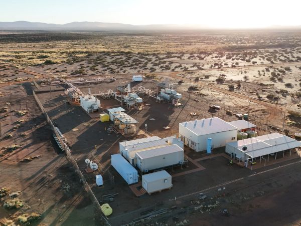 A remote industrial facility in a desert landscape during sunset.