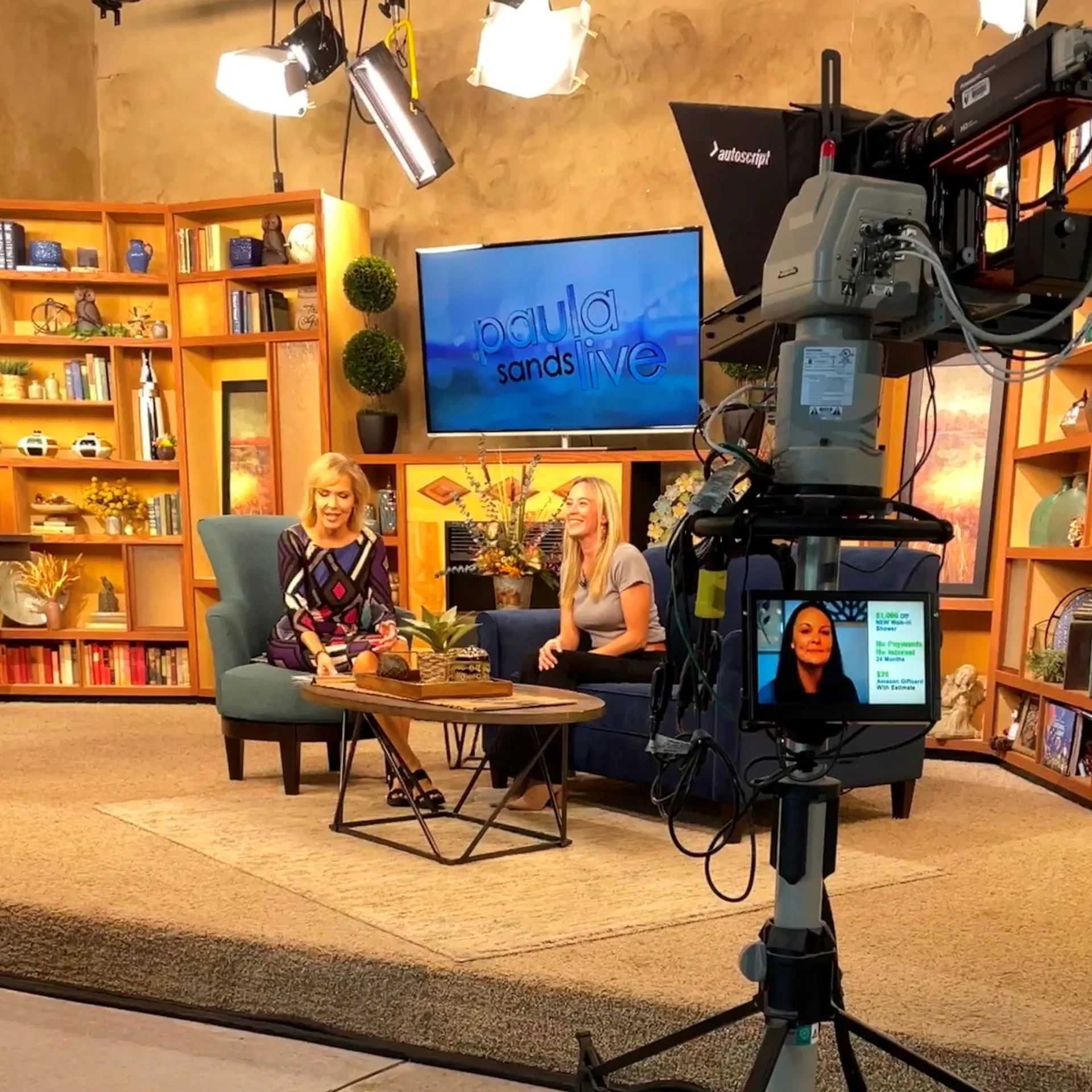 TV show set with two women seated and large camera in foreground.