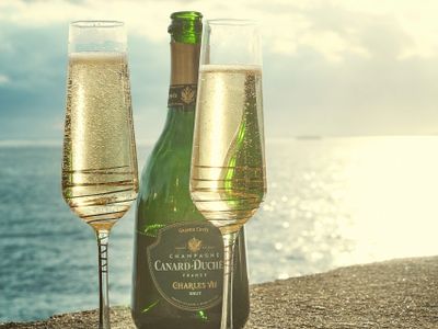 Two champagne glasses and a bottle by the sea at sunset.