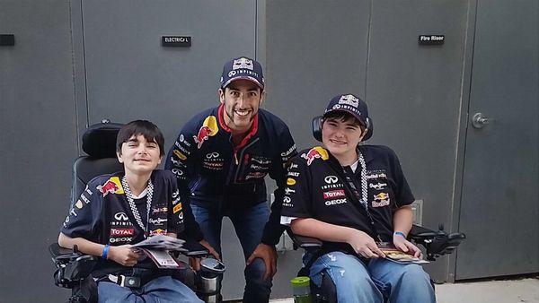 Three people, two in wheelchairs, wearing Red Bull racing shirts and caps, smiling.