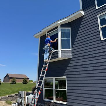 Person climbing a ladder to a window on a blue house.