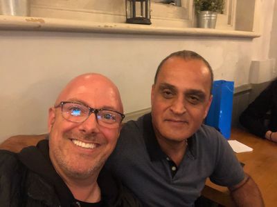 Two men smiling indoors at a wooden table.