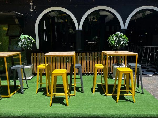 Outdoor seating area with yellow and gray stools and modern tables on green artificial grass.