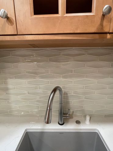 Modern kitchen sink with stainless steel faucet and textured tile backsplash.