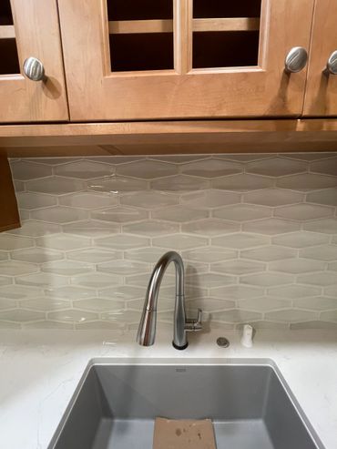 Modern kitchen sink with stainless steel faucet and textured tile backsplash.
