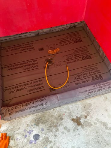 Red-walled shower pan lined with protective PVC material and a yellow pipe in the center.