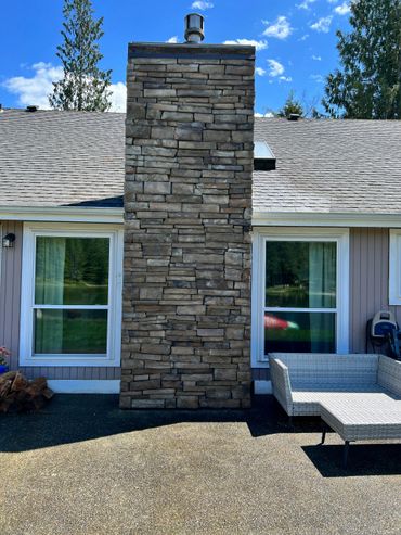 Stone chimney centered between two windows on a house patio.