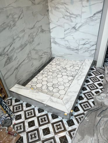 Marble-tiled shower base with hexagonal floor pattern in a bathroom under renovation.