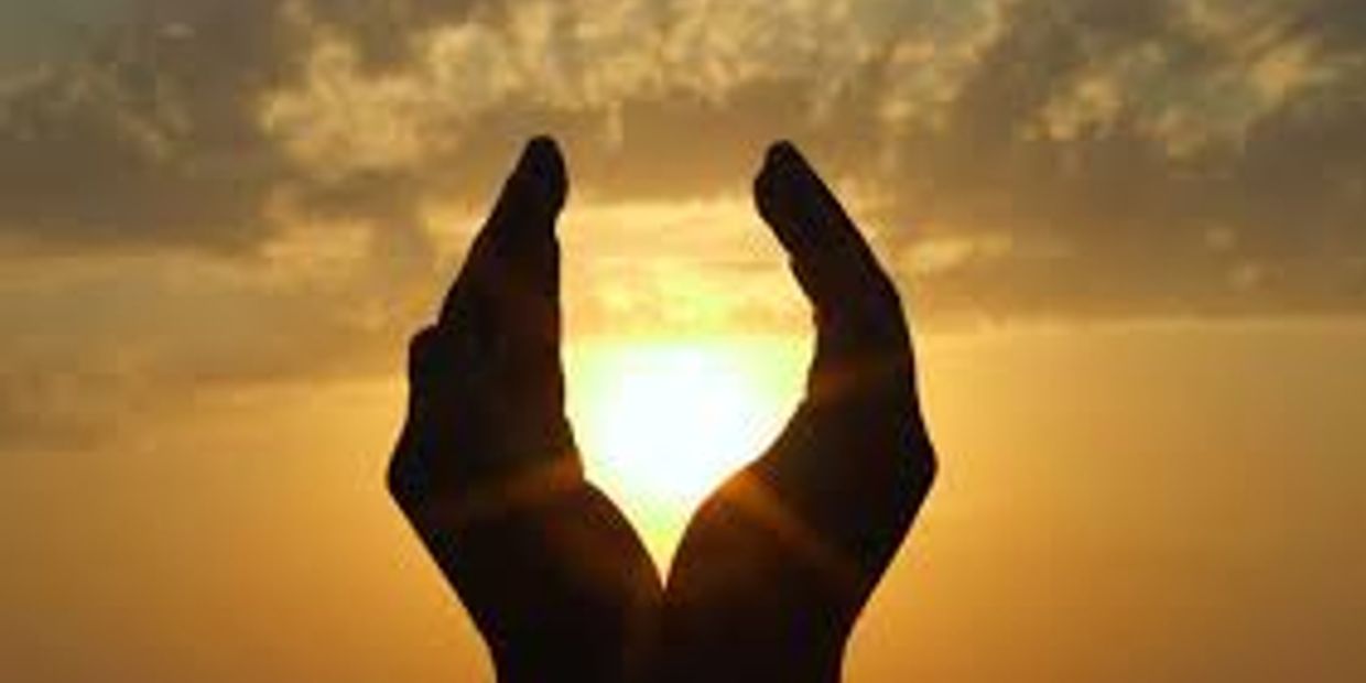 Hands framing the sun at sunset.