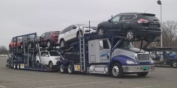 Car carrier truck loaded with multiple SUVs in a parking lot.