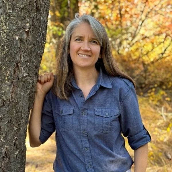 Woman smiling while leaning on a tree in autumn.