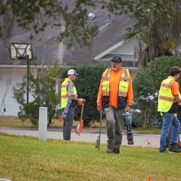Workers in safety vests surveying a grassy area with equipment.