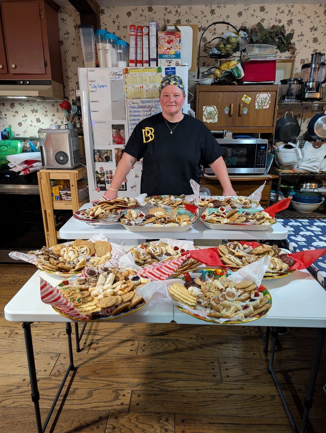 A woman stands behind a table filled with assorted homemade cookies on festive plates.
