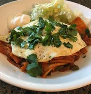 Homemade Chilaquiles topped with a fried egg, cilantro, iceberg lettuce, and a dollop of sour cream.