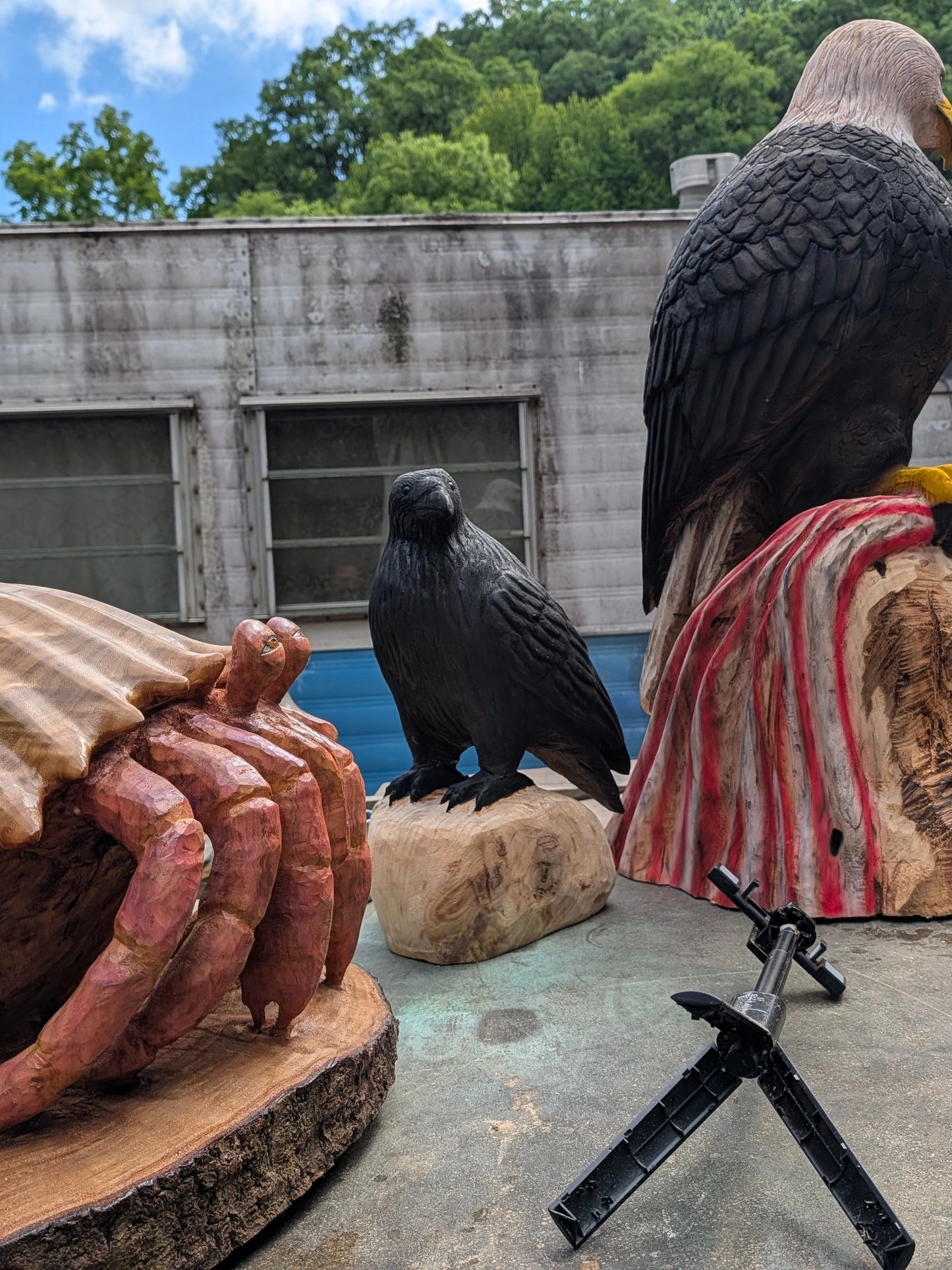 Wooden carvings of birds and a lobster outdoors.
