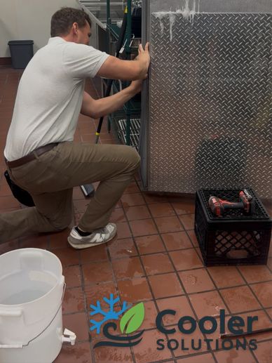Technician repairing a commercial cooler in a kitchen setting.