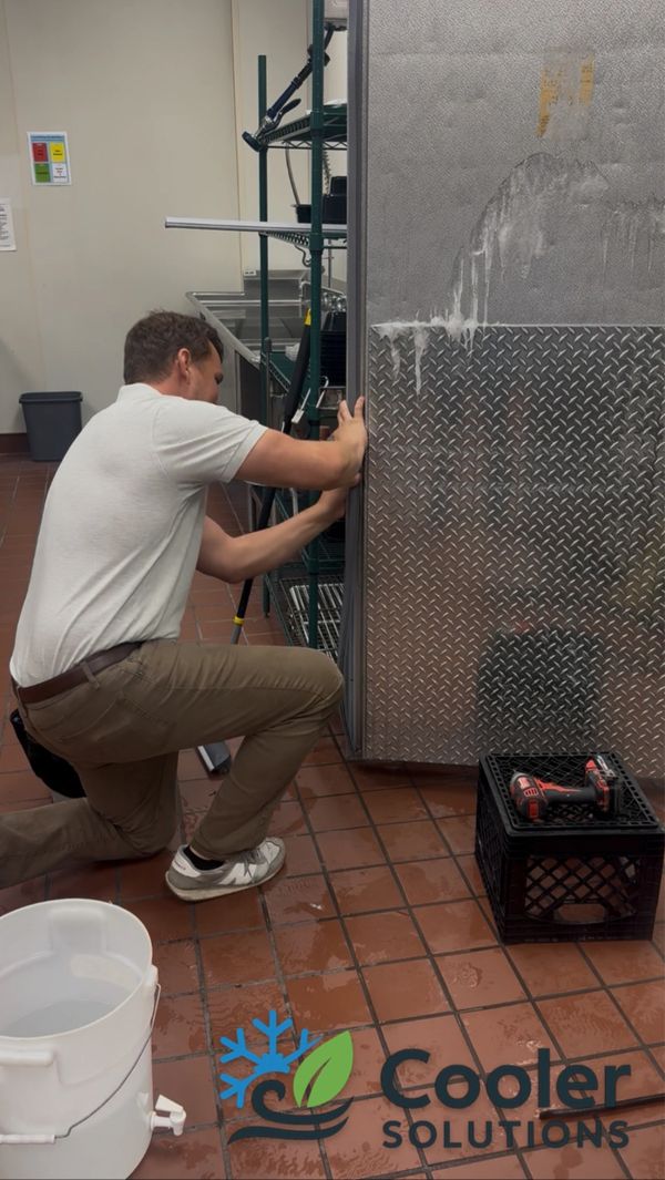 Technician repairing a commercial cooler in a kitchen setting.
