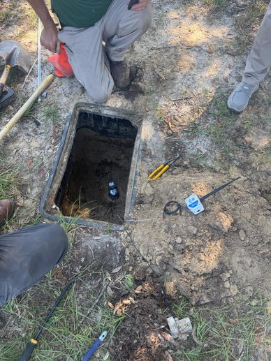 Workers inspecting an open ground utility box with tools and devices around.