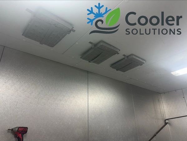 Industrial ceiling cooling units installed in a metal-paneled room.
