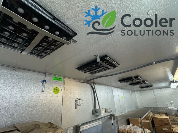 Interior of a refrigerated storage room with cooling panels on the ceiling and shelves filled with boxes and bread.