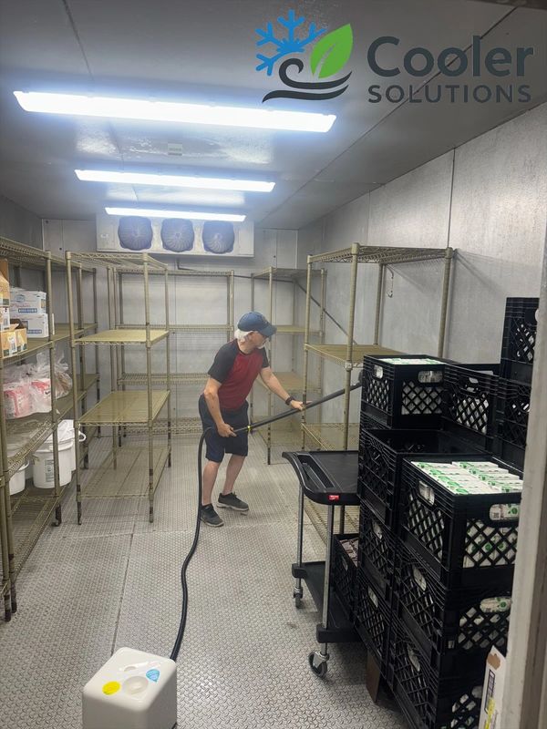 Man cleaning an industrial cooler room with a hose.