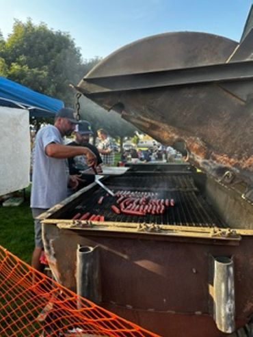 Two men grilling sausages outdoors at Warden Community Days