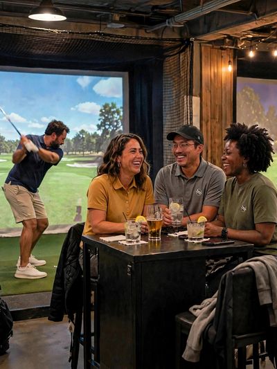 Group enjoying drinks by an indoor golf simulator.