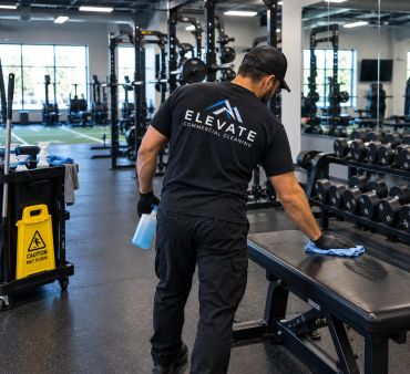 A cleaner sanitizes a bench in a gym.