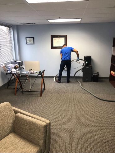 Man cleaning office carpet with vacuum cleaner.