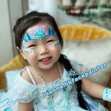 Young girl with intricate blue face paint and matching dress smiles joyfully.
