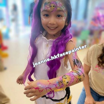 A smiling girl with colorful face and arm paint, and purple hair extensions.