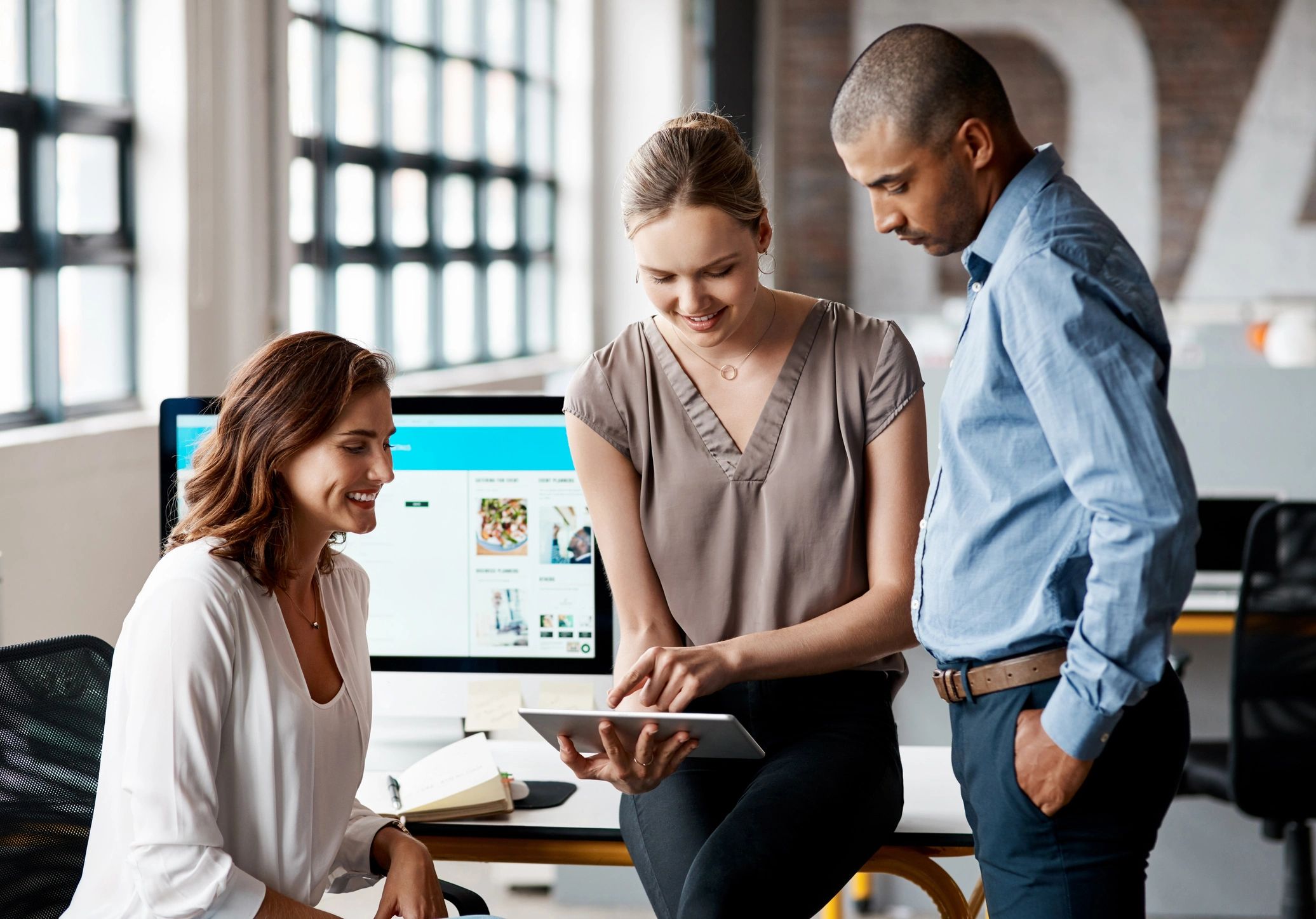 Three professionals engage in a discussion, examining a tablet, with a computer