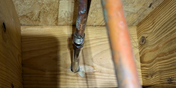 Copper and metal pipes installed through wooden framing and plywood.