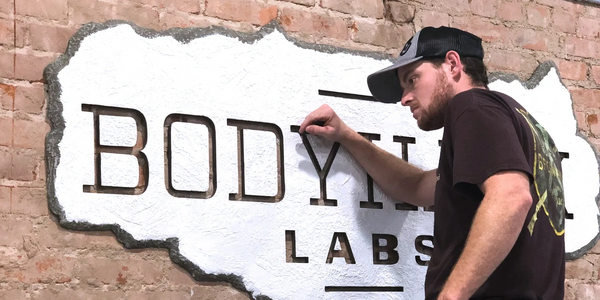 Installing a white sign on a brick wall that says Body Hack Labs