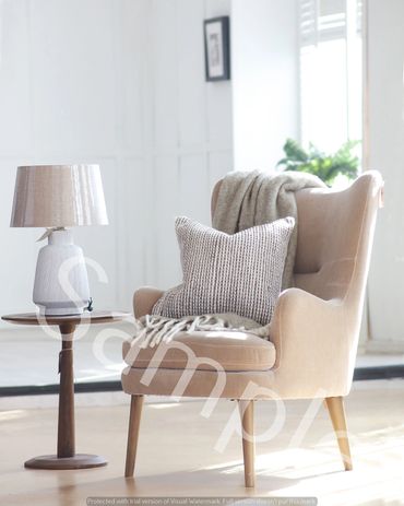 Cozy beige armchair with a textured pillow and throw blanket beside a wooden side table with a lamp.
