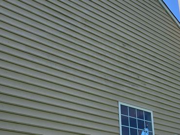 Side view of a beige house with two windows and a chimney against a clear blue sky.