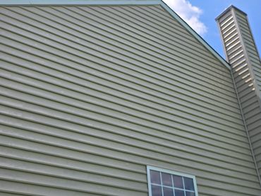 Side of a house with beige siding, a window, and a chimney under a blue sky.