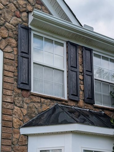 Stone house facade with white bay window and black shutters.