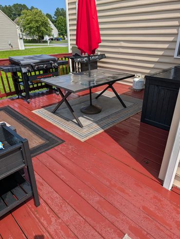 Outdoor patio with red deck, table, umbrella, and grills.