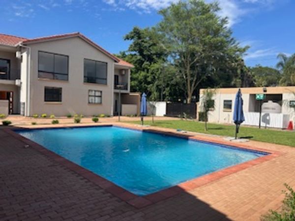 Clear blue pool in a sunny residential courtyard with umbrellas.